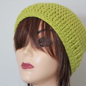 May include: A lime green crochet beanie hat. The hat is made of a textured yarn and has a ribbed design. The hat is shown on a mannequin head with brown hair and red lipstick.