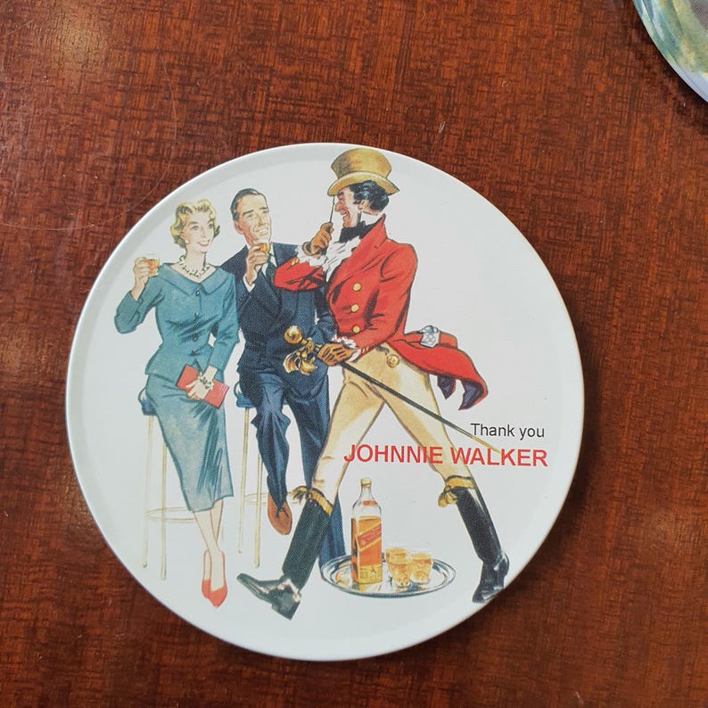 May include: Round white decorative plate featuring a vintage illustration of three people and a man in a red coat, with the text "Thank you JOHNNIE WALKER". The plate has a glossy finish and a brown rim.