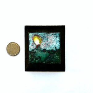 May include: A small, framed artwork with a blue, green, and yellow abstract design. The artwork is framed in black.