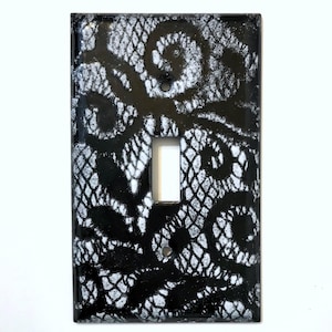 May include: Black and white decorative light switch cover with a lace design. The cover has a glossy finish and a rectangular shape with a single toggle switch opening. The lace pattern is white against a black background.