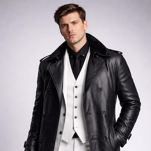 Op de afbeelding: Een lange zwarte leren trenchcoat met een dubbele rij knopen, gedragen over een wit vest en een zwart overhemd. De outfit omvat een witte broek en zwarte handschoenen. De jas heeft een reverskraag en een ceintuur.