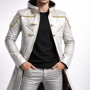 May include: A silver-gray long coat with gold accents and decorative clasps. The coat has a quilted shoulder design and a hood. The person is wearing a black sweater and gray pants.