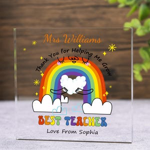 May include: A clear acrylic block with a colorful rainbow design. The text reads "Mrs. Williams, Thank You for Helping Me Grow, Best Teacher, Love From Sophia." The rainbow has a smiling face and is holding a white heart.