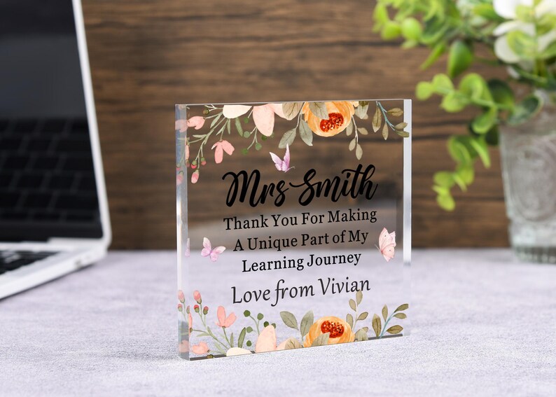 May include: A clear acrylic block with floral and butterfly accents. The block is inscribed with the words "Mrs. Smith, Thank You For Making A Unique Part of My Learning Journey, Love from Vivian."