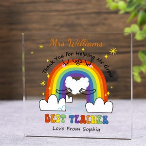May include: A clear acrylic block with a colorful rainbow design. The text reads "Mrs. Williams, Thank You for Helping Me Grow, Best Teacher, Love From Sophia." The rainbow has a smiling face and is holding a white heart.