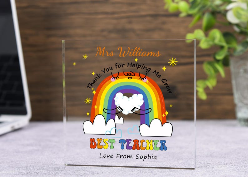 May include: A clear acrylic block with a colorful rainbow design. The text reads "Mrs. Williams, Thank You for Helping Me Grow, Best Teacher, Love From Sophia." The rainbow has a smiling face and is holding a white heart.