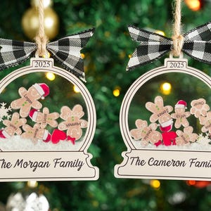 May include: Two Christmas ornaments with a clear globe design, featuring gingerbread people with names and Santa hats. Each ornament has a black and white checkered bow and the year 2025. The text on the bottom reads "The Morgan Family" and "The Cameron Family".