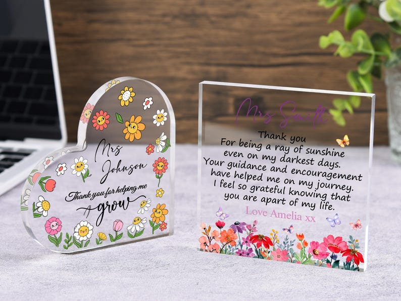 May include: Two clear acrylic plaques. One is heart-shaped with floral designs and the text "Mrs. Johnson, Thank you for helping me grow." The other is rectangular with a floral border and the text "Thank you...Love Amelia xx."