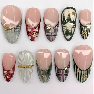 May include: A collection of ten artificial nails with various designs. The nails feature a nude base with different accents, including gold snowflakes, stars, plaid patterns, and a winter landscape. Some nails have a French tip design with a gold border.