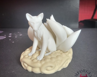 Puede incluir: Una figura de zorro blanco con múltiples colas, sentado sobre una base en forma de nube de color crema. El zorro está en posición sentada, con las orejas erguidas. Es probable que la figura sea un objeto decorativo o de colección.