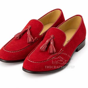 May include: A pair of red suede loafers with tassel details. The shoes have a rounded toe, white stitching, and a leather sole. The interior is a light tan color. The shoes are displayed on a white background.