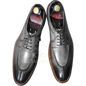 Peut inclure: Une paire de chaussures de ville en cuir gris avec un bout rapporté. Les chaussures ont une fermeture à lacets et une semelle marron. L'image comprend le texte "THECRAFTEDSTEP" et "MADE LEATHER SHOES".