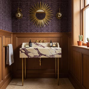 May include: A bathroom interior featuring a marble sink with gold legs and fixtures. The sink has a cream base with purple veining. A gold sunburst mirror hangs above the sink, and the walls are paneled with wood and patterned wallpaper.