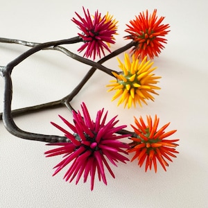 Può includere: Un ramo decorativo in metallo con ornamenti a forma di stella appuntita nei colori fucsia, arancione e giallo. Il ramo marrone scuro si staglia su uno sfondo bianco. Gli ornamenti misurano circa 5 cm di diametro.