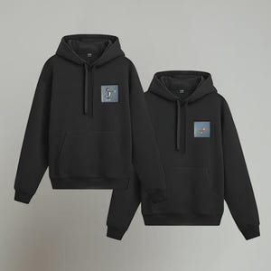 May include: Two black hoodies with a front pocket and a hood. Each hoodie has a small square patch on the chest with a graphic design. The hoodies are displayed against a gray background.