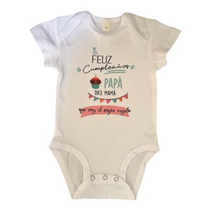 Könnte beinhalten: Weißer Baby-Body mit kurzen Ärmeln. Der Body trägt den Text "Feliz Cumpleaños Papá" mit einer Cupcake-Illustration und einem Banner mit der Aufschrift "que soy el mejor regalo".