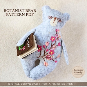May include: A light blue felt bear holding a brown book with the word "BOTANY" on it. The bear has embroidered pink flowers and a "Beginner Friendly" badge. Text on the image reads "BOTANIST BEAR PATTERN PDF" and "DIGITAL DOWNLOAD | NOT A FINISHED ITEM."
