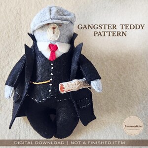 May include: A felt teddy bear dressed as a gangster, wearing a gray cap, black suit, and red tie. The bear holds a rolled paper and the text "GANGSTER TEDDY PATTERN" is displayed.