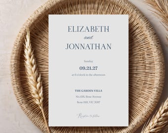 May include: A wedding invitation with the names "ELIZABETH and JONNATHAN" in a serif font. The invitation is on a light gray background, with the date and time of the event. The invitation is placed on a woven tray with dried wheat.