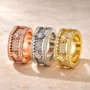 May include: Three rings in rose gold, silver, and gold. Each ring features a gear-like design with embedded gemstones and a central, larger gem. The rings are displayed side-by-side, showcasing their intricate details.