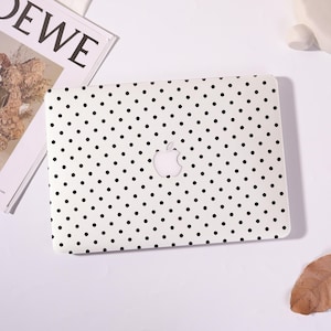 Op de afbeelding: Een witte harde beschermhoes voor een laptop met een herhalend patroon van kleine zwarte stippen. De hoes is ontworpen voor een laptop en heeft een centrale uitsparing die het zilveren Apple-logo op het deksel van het apparaat blootlegt.