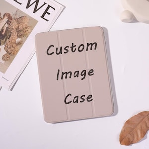 May include: A light beige tablet case with a tri-fold design and the black text Custom Image Case printed on the front. The case has a smooth, matte finish and vertical creases that allow it to fold into a stand for the electronic device.