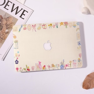 May include: A cream-colored laptop case adorned with a border of colorful, whimsical illustrations. The design includes flowers, bows, hearts, and fruits. The Apple logo is visible in the center.