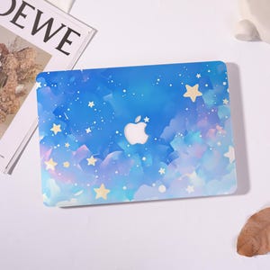 May include: A laptop hard shell case featuring a blue and purple watercolour-style sky pattern with scattered yellow stars and white dots. The centre of the case displays a cutout for the Apple logo, revealing the silver metallic surface underneath.