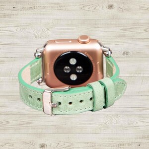K&ouml;nnte beinhalten: Ros&eacute;goldene Smartwatch mit hellgr&uuml;nem Lederarmband. Das Armband hat eine silberne Schnalle und ist mit silbernen Verbindern an der Uhr befestigt. Das Zifferblatt der Uhr ist schwarz mit drei kreisf&ouml;rmigen Sensoren.
