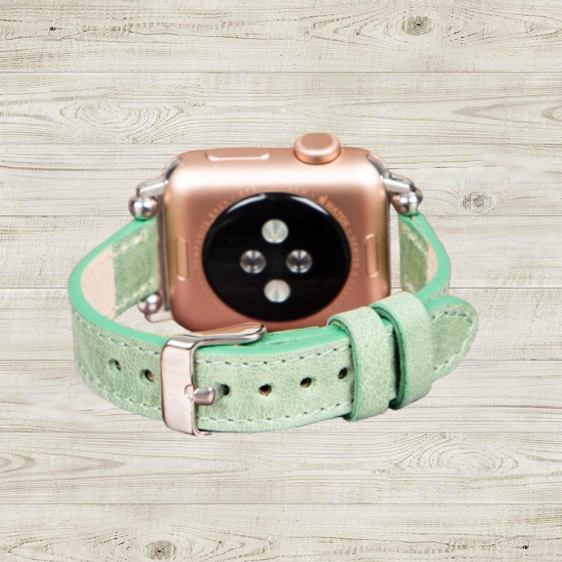 K&ouml;nnte beinhalten: Ros&eacute;goldene Smartwatch mit hellgr&uuml;nem Lederarmband. Das Armband hat eine silberne Schnalle und ist mit silbernen Verbindern an der Uhr befestigt. Das Zifferblatt der Uhr ist schwarz mit drei kreisf&ouml;rmigen Sensoren.