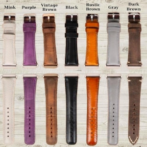 May include: A collection of watch bands in various colors, including green, mink, purple, and brown. Each band features a buckle and stitching details. The bands are displayed on a light wood-grain surface.