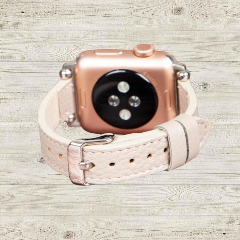 K&ouml;nnte beinhalten: Ros&eacute;goldene Smartwatch mit cremefarbenem Lederarmband. Die Uhr hat einen schwarzen Sensor auf der R&uuml;ckseite und eine silberne Schnalle. Das Armband ist mit kleinen L&ouml;chern perforiert.