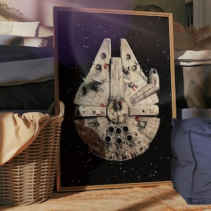 Puede incluir: Un cuadro enmarcado de la nave espacial Halcón Milenario sobre un fondo estrellado. La nave espacial está detallada en tonos blancos, grises y rojos, con una sección central circular y una cabina distintiva. El cuadro se exhibe en una habitación con una cesta tejida y un puf azul.