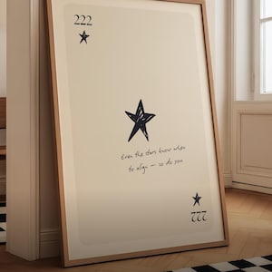 May include: A framed art print with a cream-colored background and a wooden frame. The print features a large black star, smaller stars, and the numbers 222 and 777. The text "Even the stars know when to align - so do you" is written in cursive.