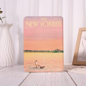 May include: A rectangular decorative item with a vintage "The New Yorker" cover illustration. The artwork shows a person fishing with a dog in water under a sunset. The text "THE NEW YORKER" is displayed at the top.