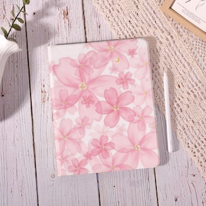 May include: A rectangular tablet case featuring a white background with a repeating pattern of translucent pink cherry blossoms. Each flower center is accented with gold glitter. A slim white stylus is positioned vertically next to the case.