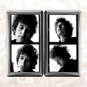 May include: A silver metal cigarette case featuring four black and white images of a man with curly hair. The images are arranged in two rows of two, with the man's face in different poses.