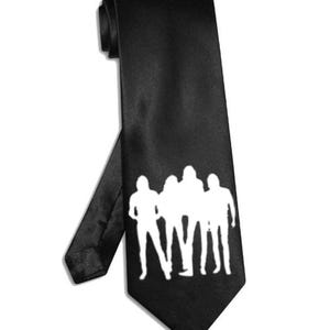Peut inclure: Cravate noire avec un motif de silhouette blanche représentant quatre personnages. La cravate est faite d'un matériau lisse et brillant, idéale pour les occasions formelles. Le design est simple mais accrocheur.