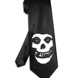 Könnte beinhalten: Schwarze Krawatte mit einem weißen Totenkopf-Design. Die Krawatte besteht aus einem glatten, glänzenden Stoff und wird vor einem weißen Hintergrund präsentiert. Das Totenkopf-Motiv ist mittig platziert und hat ein detailliertes, stilisiertes Aussehen.
