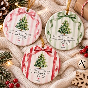 Può includere: Tre ornamenti rotondi in ceramica con un albero di Natale decorato con tessere del mahjong. Ogni ornamento presenta uno sfondo a righe rosa, verde o rosso, un nastro grafico e il testo "THE YEAR I LEARNED mahjong" con "2026".
