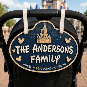 May include: An oval-shaped wooden stroller sign with a dark blue background and light wood trim. It features a castle graphic, fireworks, and four Mickey Mouse head icons. The text reads THE ANDERSONS FAMILY and WHERE MAGIC MEMORIES BEGIN.