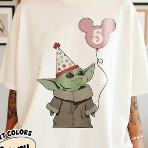 May include: Ivory-colored t-shirt featuring a cartoon character wearing a party hat and holding a pink balloon with the number 5. The t-shirt has the words "COMFORT COLORS" and "Ivory" printed on it.
