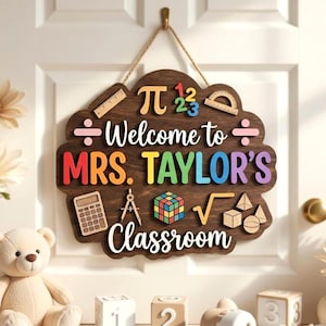 May include: A dark wood classroom sign hanging by a rope, featuring the text "Welcome to MRS. TAYLOR'S Classroom" in colorful 3D letters. It is decorated with wooden math symbols, a calculator, a compass, a cube puzzle, and geometric shapes.