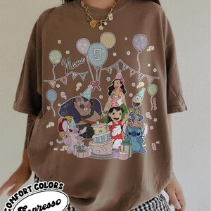 May include: Brown t-shirt featuring a colorful graphic of cartoon characters, balloons, and a birthday cake. The design includes the number 5 and the word "Name". The shirt has the words "Comfort Colors Espresso" in a circular design.