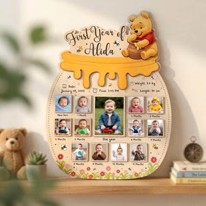 Könnte beinhalten: Ein hölzernes Meilenstein-Board in Honigtopf-Form mit Winnie Puuh, betitelt First Year of Alida. Es enthält zwölf Fotofelder für die monatliche Entwicklung, Geburtsdaten wie 09. Januar 2025, 3,2 kg, 50 cm, verziert mit Bienen und Blumen.