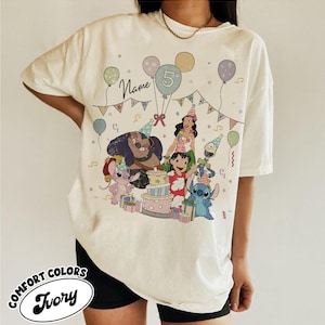May include: Ivory Comfort Colors t-shirt featuring a colorful birthday party design with cartoon characters, balloons, and a cake. The design includes the number 5 and the word "Name". The shirt is a relaxed fit.