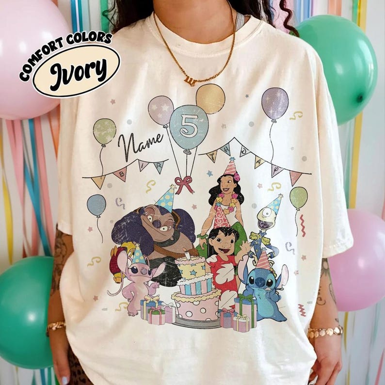 May include: Ivory Comfort Colors t-shirt featuring a colorful birthday party design with cartoon characters, balloons, and a cake. The design includes the text "Name" and the number "5". The shirt has a relaxed fit.