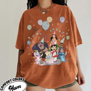 May include: Orange Comfort Colors t-shirt featuring a birthday party scene with cartoon characters, balloons, and a cake. The number 5 is displayed on a balloon. The word "Name" is written on the shirt.