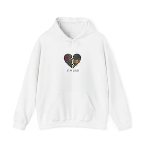 Puede incluir: Sudadera con capucha blanca con bolsillo delantero y cordón. El diseño presenta un gráfico de corazón dividido con un patrón de cuadros y el texto "STAY LOUD" en negro.