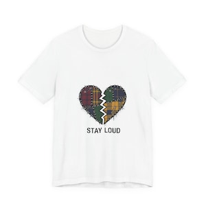 May include: White t-shirt featuring a patchwork heart design in shades of red, green, yellow, and blue. The heart is split in two, with the text "STAY LOUD" printed below in black.